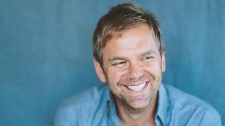 Man smiling in front of a blue background.