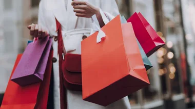 Person holding colorful shopping bags in an outdoor market.