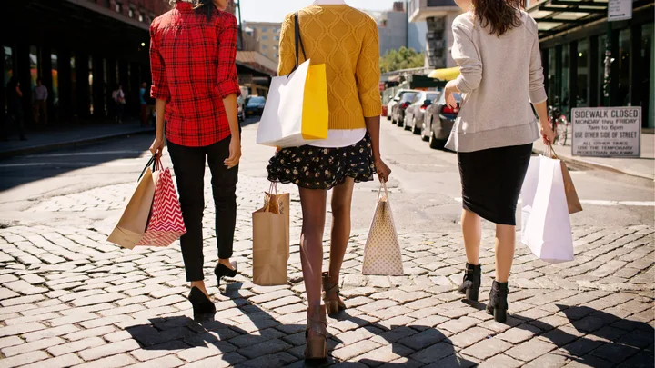 Three women walking on a cobblestone street carrying shopping bags.