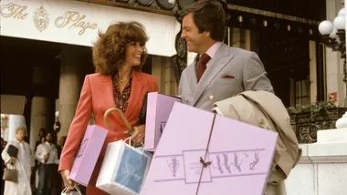 A man and woman happily holding shopping bags outside The Plaza Hotel.
