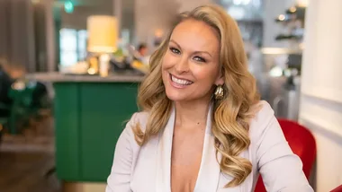 Smiling woman with long, wavy blonde hair in a bright indoor setting.