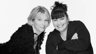 Two women smiling warmly, one with short hair and another with a ponytail. Black and white photo on a plain background.