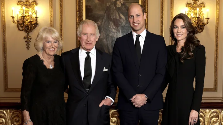 Four well-dressed individuals standing in a formal room with ornate decor and paintings.