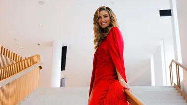 Woman in a red dress smiling on a staircase, inside a modern, well-lit building.