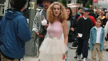 Carrie Bradshaw in a pink tank top and tulle skirt walking on a busy city street.