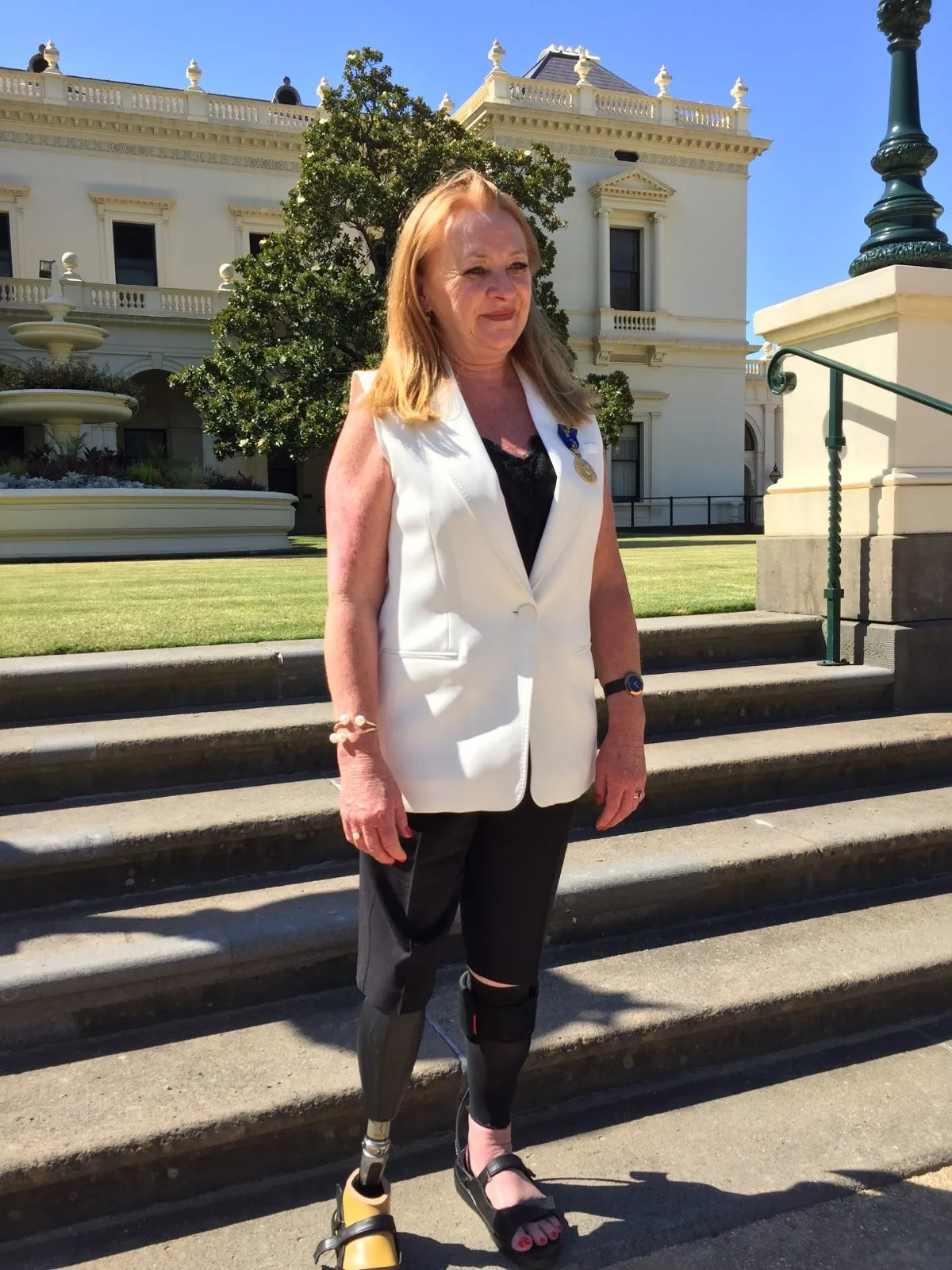 Melissa wears formal black trousers which reveal her prosthetic leg and a white waistcoat on the day she becomes a Member of the Order of Australia (AM).