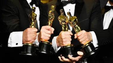 Close-up of four people holding Oscar statuettes, wearing black tuxedos.