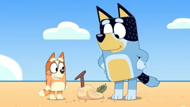 Two animated dogs on a beach, with a sand sculpture shaped like a bird in front of them.