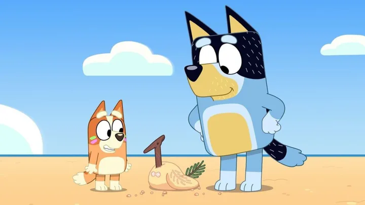 Two animated dogs on a beach, with a sand sculpture shaped like a bird in front of them.