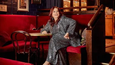 A person in a sparkling dress sits in a cozy, dimly lit restaurant booth, showcasing an animated expression.