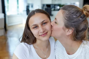 Mother kissing teenage daughter on the cheek at home