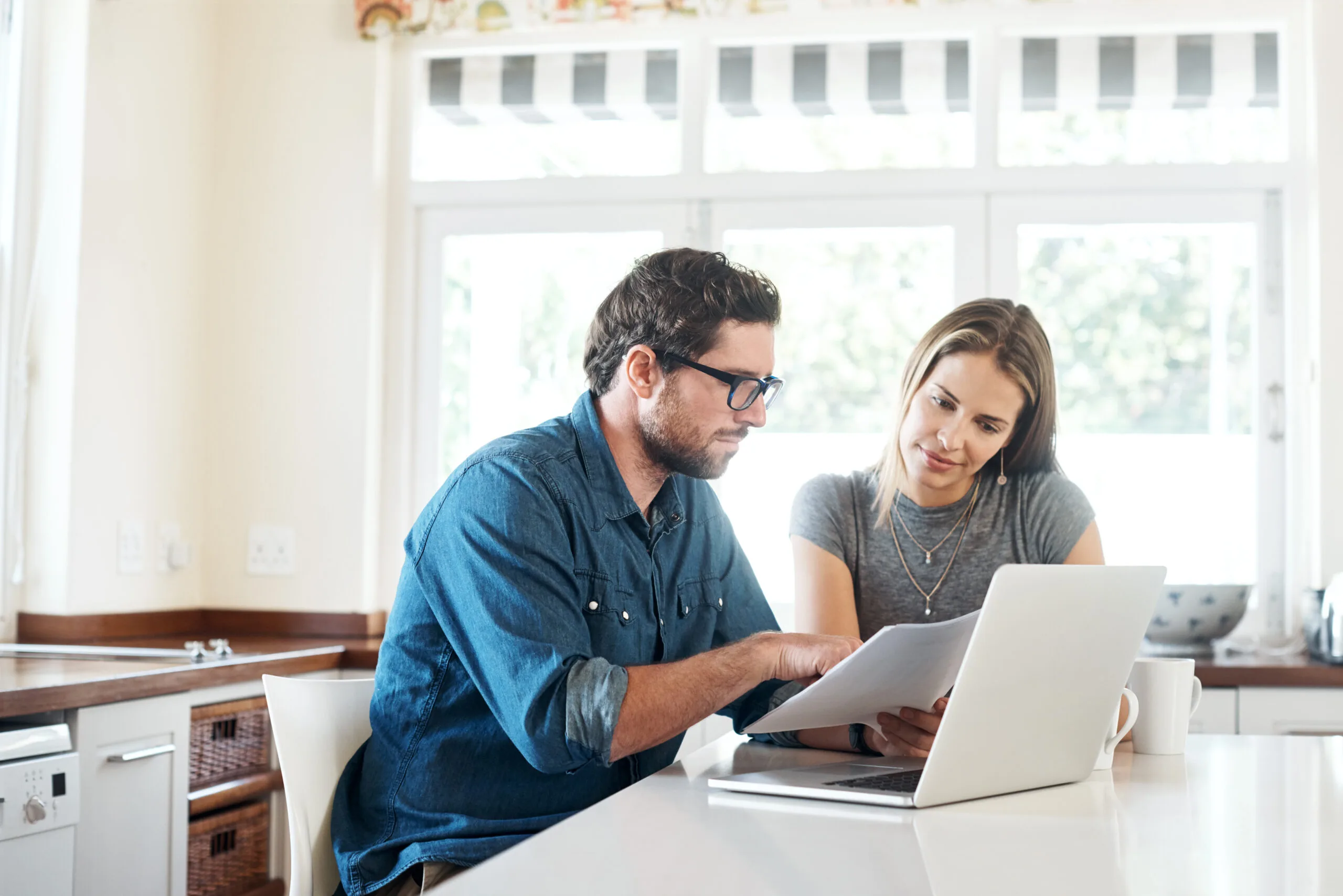 man and woman sit at a table looking at a laptop - discuss finances