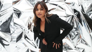 Woman in black outfit posing in front of a shiny, crumpled metallic background.