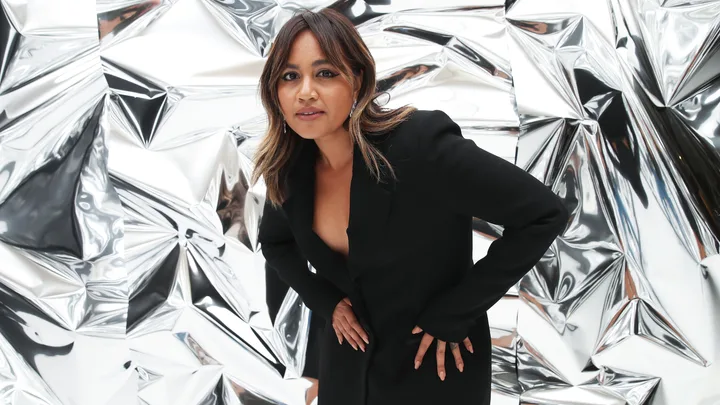 Woman in black outfit posing in front of a shiny, crumpled metallic background.