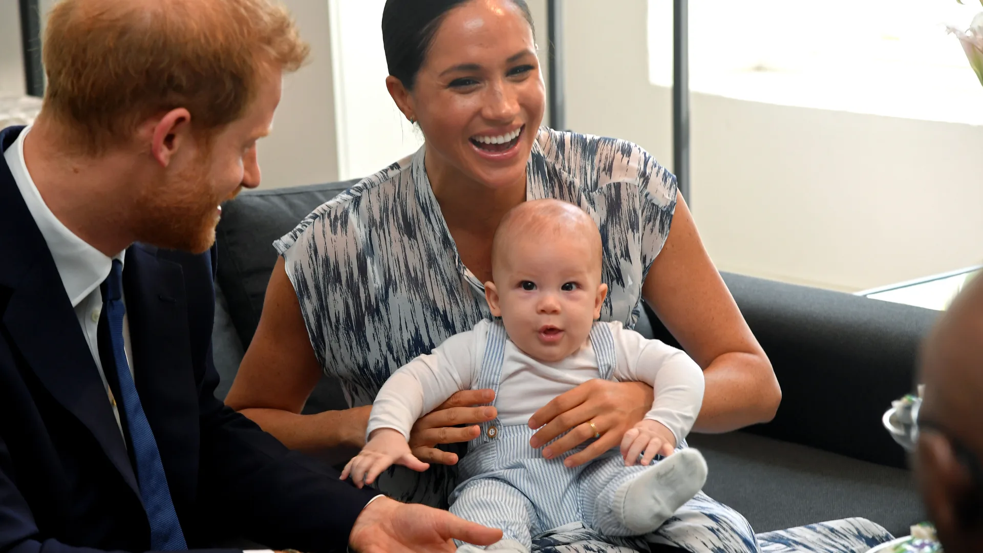 A man and woman smiling at each other while holding a baby on their lap indoors.
