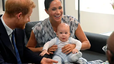 A man and woman smiling at each other while holding a baby on their lap indoors.