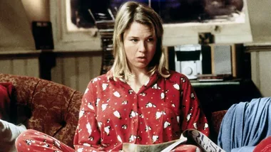 Person in red pajamas with penguin print sitting on a couch, holding a magazine, with a surprised expression.