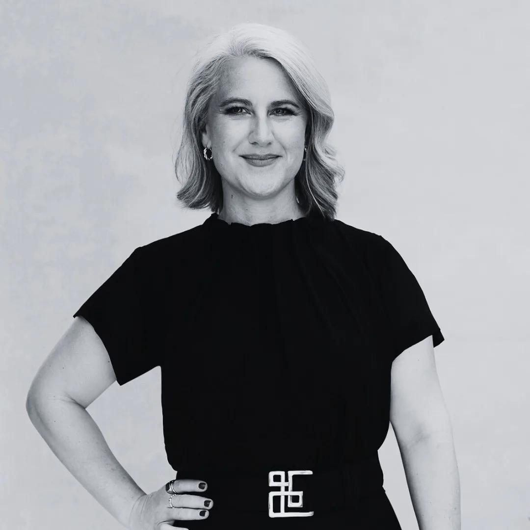 Black and white portrait of a smiling woman with shoulder-length hair, wearing a black dress and a decorative belt.