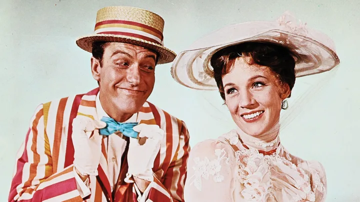 Man and woman in colorful costumes smiling, woman wears a white hat, scene from classic film "Mary Poppins."