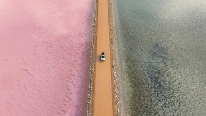 Aerial view of a car driving on a road separating pink and gray salt lakes in Australia.