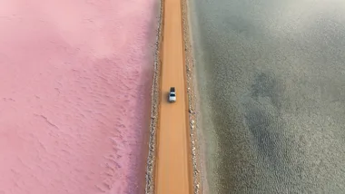Aerial view of a car driving on a road separating pink and gray salt lakes in Australia.