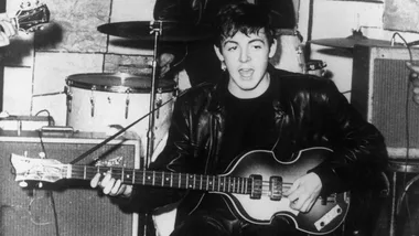 Young man in leather jacket playing a Hofner bass guitar, 1960s band rehearsal setting.