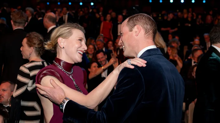 Two people smiling and interacting warmly at the BAFTA Awards, surrounded by a crowd in formal attire.