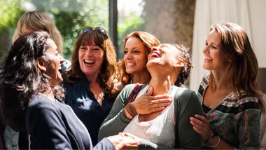 Group of women laughing and enjoying each other's company in a bright room.