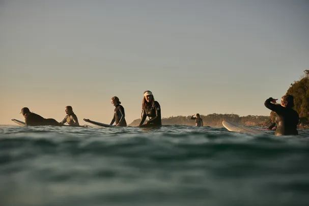 A group of Australian female surfers on their surfboards in the water.