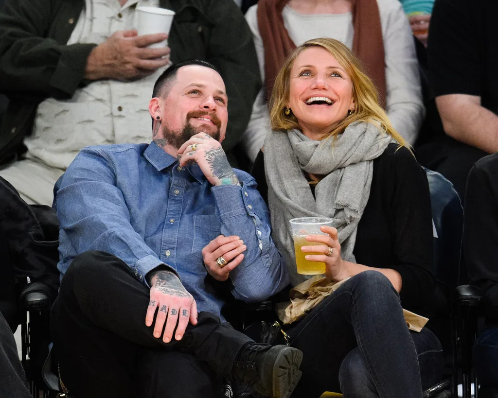 A man and a woman sit closely at a sports event, smiling and enjoying drinks.