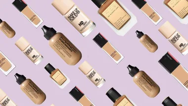 Various foundation bottles from brands like Make Up For Ever, MAC, and Pat McGrath against a light purple background.