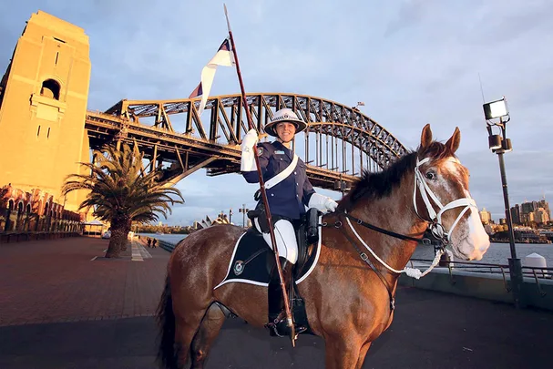 Mounted police officer in uniform on horseback in front of the Sydney Harbour Bridge at sunrise.