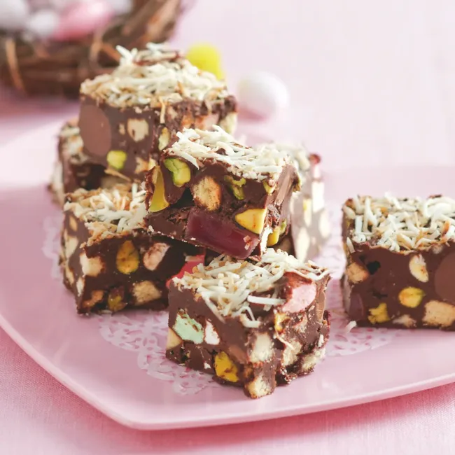 Rocky road squares with marshmallows, nuts, and coconut, stacked on a pink plate.