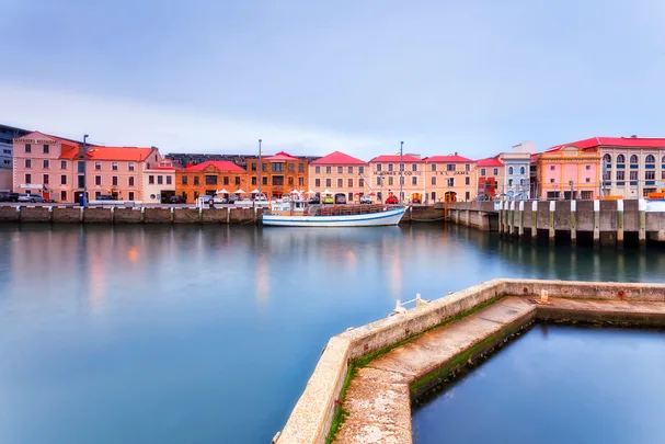 Historic waterfront in Hobart, Tasmania, with colorful buildings and a docked boat under a cloudy sky.