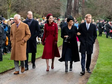 A group of well-dressed people walking on a path, surrounded by a crowd, in an outdoor setting.