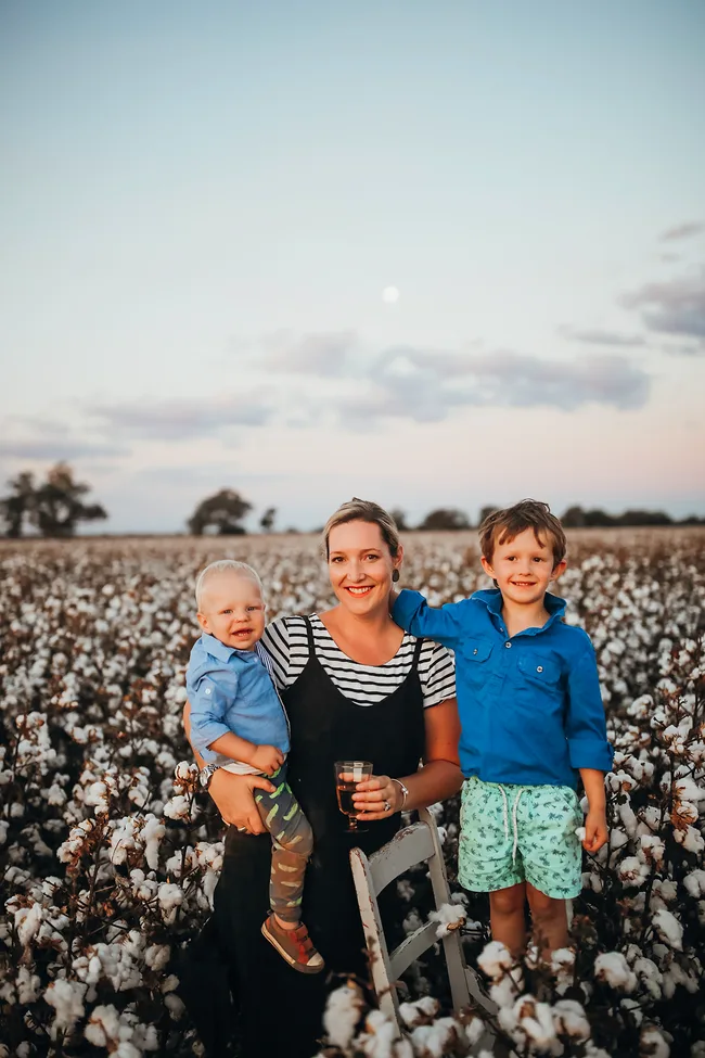 A woman with two children in a cotton field at sunset.