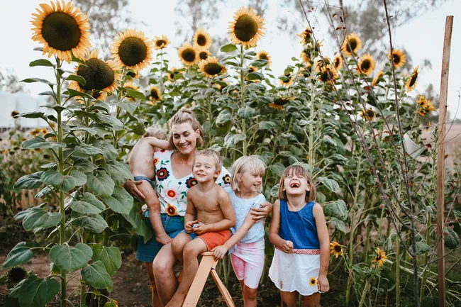 Mother and three kids smiling in a sunflower garden.