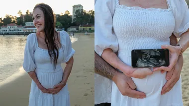 Pregnant woman in white dress smiles by the beach; phone shows ultrasound; partner hugs her from behind.