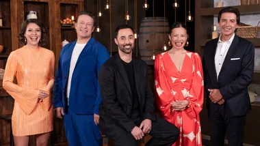 Five people dressed formally stand together, smiling, in a warmly lit room with hanging lights and wooden decor.