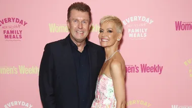 A man and woman smiling at an event in front of a pink "Women's Weekly" backdrop.