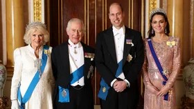 Four elegantly dressed individuals pose together in a grand room, wearing formal attire and medals.