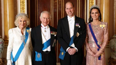 Four elegantly dressed individuals pose together in a grand room, wearing formal attire and medals.