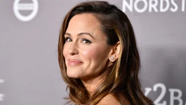 Woman smiling at a Nordstrom event with subtle makeup and diamond earrings, against a gray backdrop.