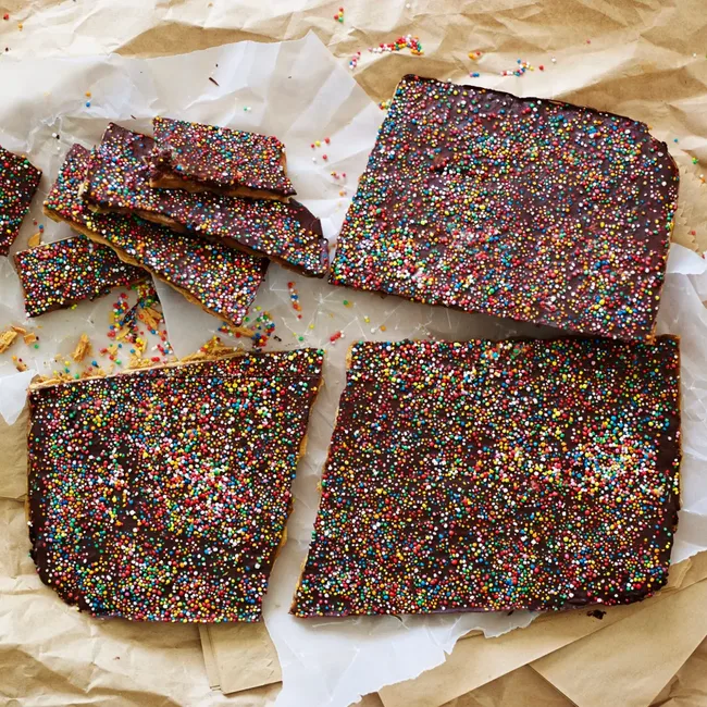 Broken pieces of chocolate bark covered with colorful sprinkles on parchment paper.