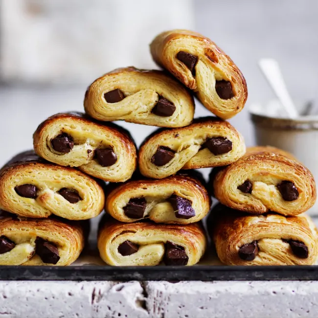 Stack of chocolate croissants on a tray with a blurred background.