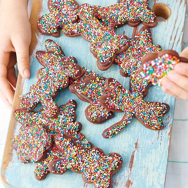 Chocolate cookies shaped like animals, topped with colorful sprinkles, on a blue wooden board.