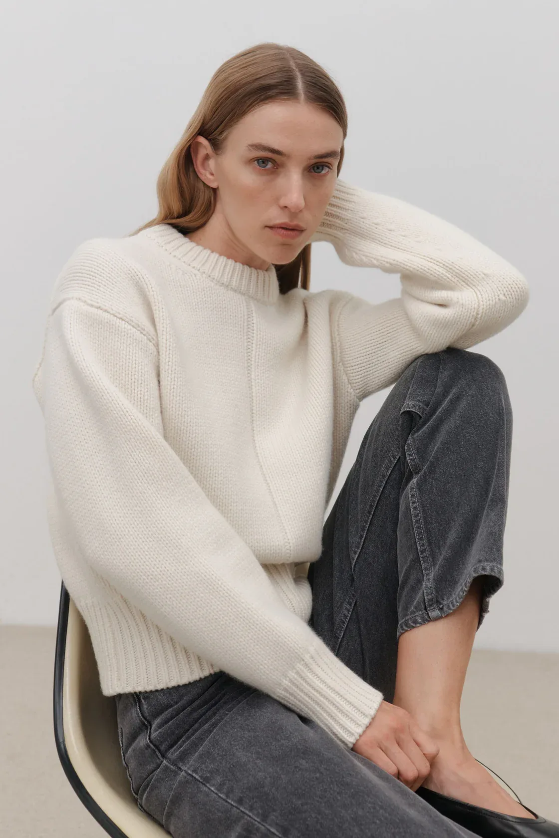 Female model wearing Australian knitwear brand Assembly, sitting on chair.