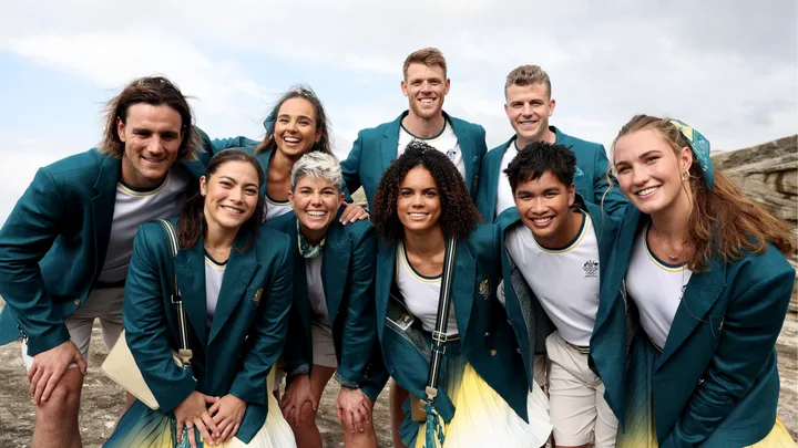 Group of smiling athletes in green Olympic blazers standing together outdoors.