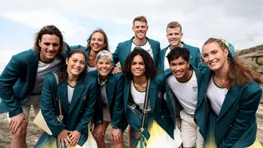 Group of smiling athletes in green Olympic blazers standing together outdoors.