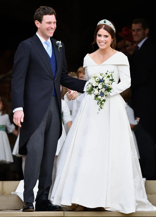 Bride in white gown holding flowers and groom in suit standing smiling together after a wedding ceremony.